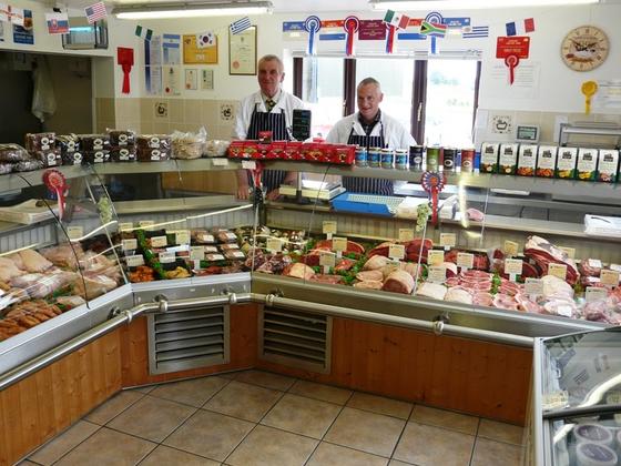 Two butchers stood behind the display counter showcasing their products